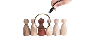 Hand holding magnifying glass over wooden figures representing deep candidate screening and talent selection