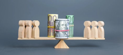 Wooden figures balanced with rolled banknotes on scale representing competitive fair pay and talent compensation