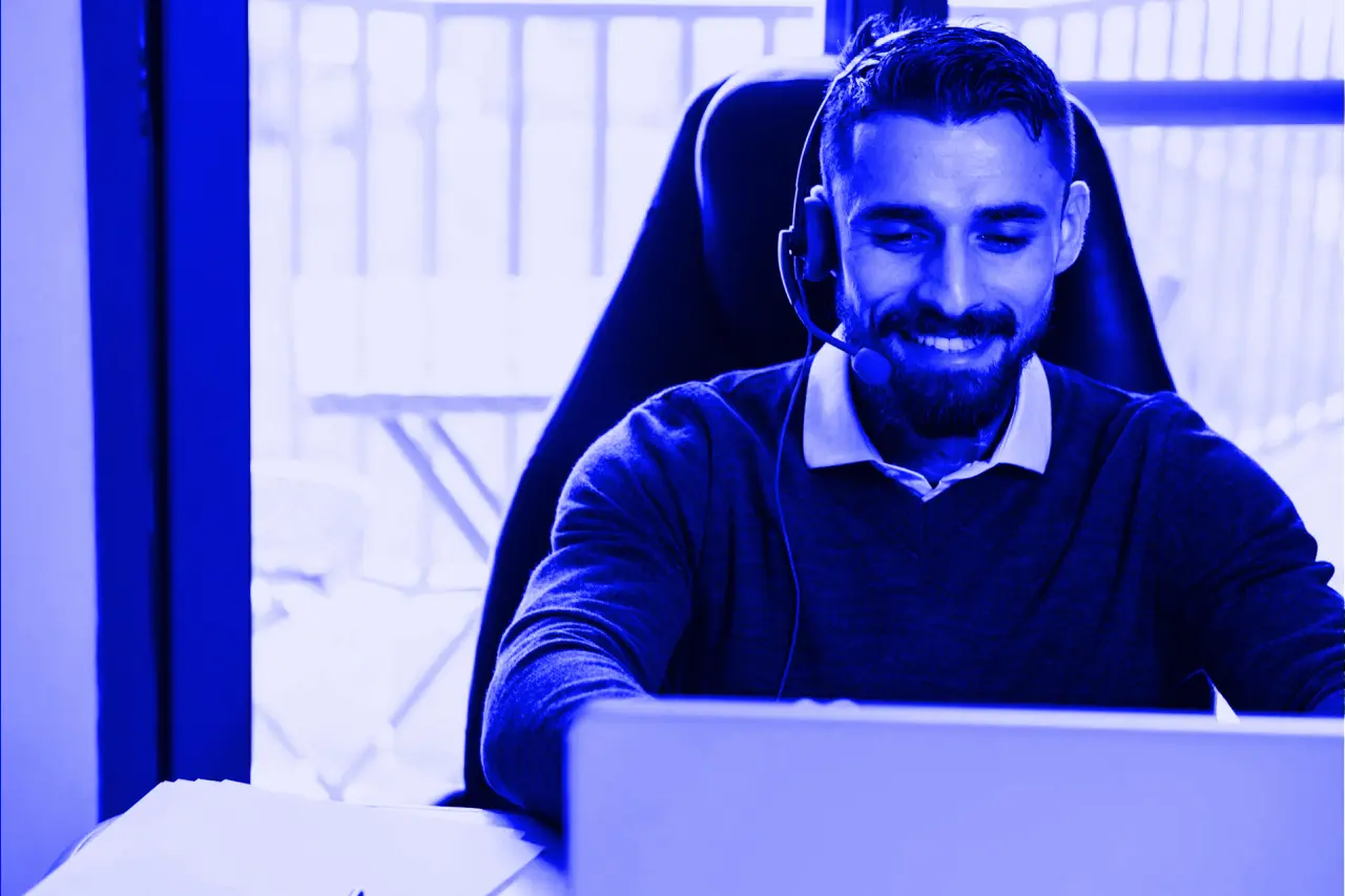 Smiling customer support agent wearing a headset and working on a laptop