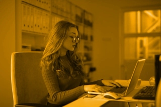 Remote worker with long hair and glasses working on a laptop at an office desk